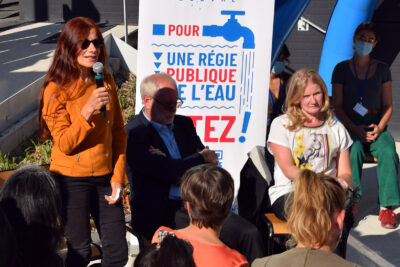 Une femme face à un kakemono de la régie publique de l'eau, parle au public dans son micro - Agrandir l'image 4 sur 9, fenêtre modale